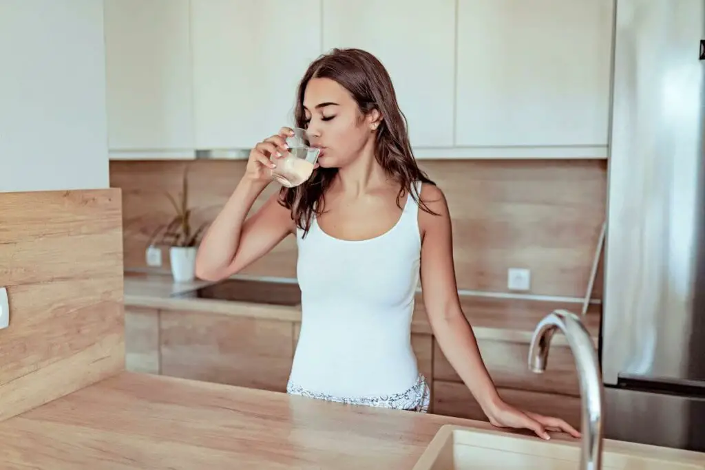 A woman enjoying a refreshing glass of water in her kitchen.