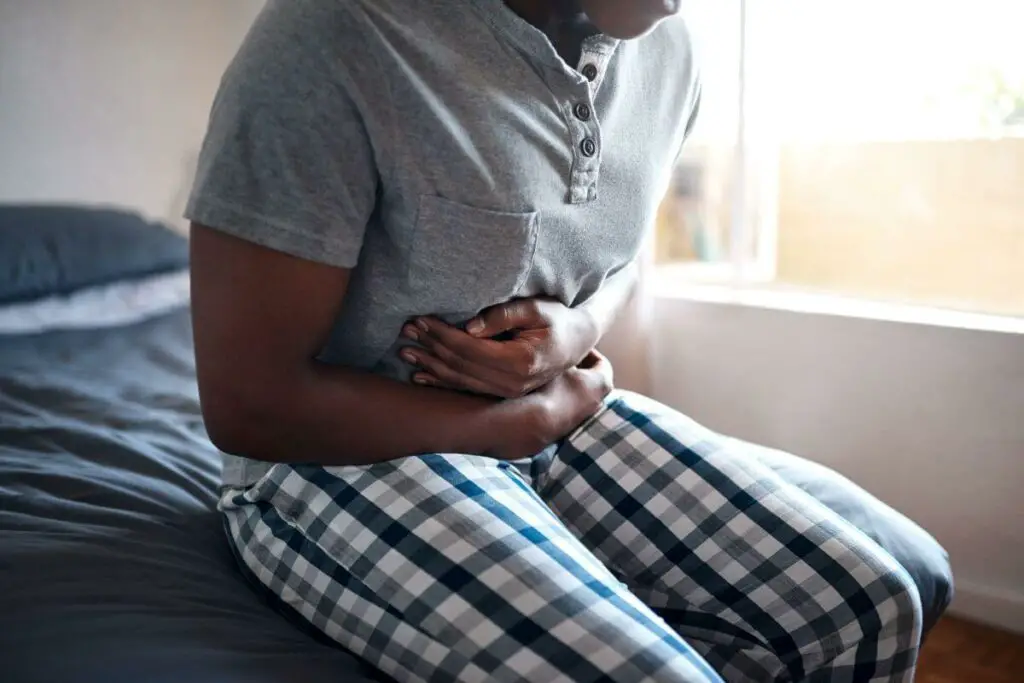 A person clutching his stomach in pain while reaching for ibs medication.
