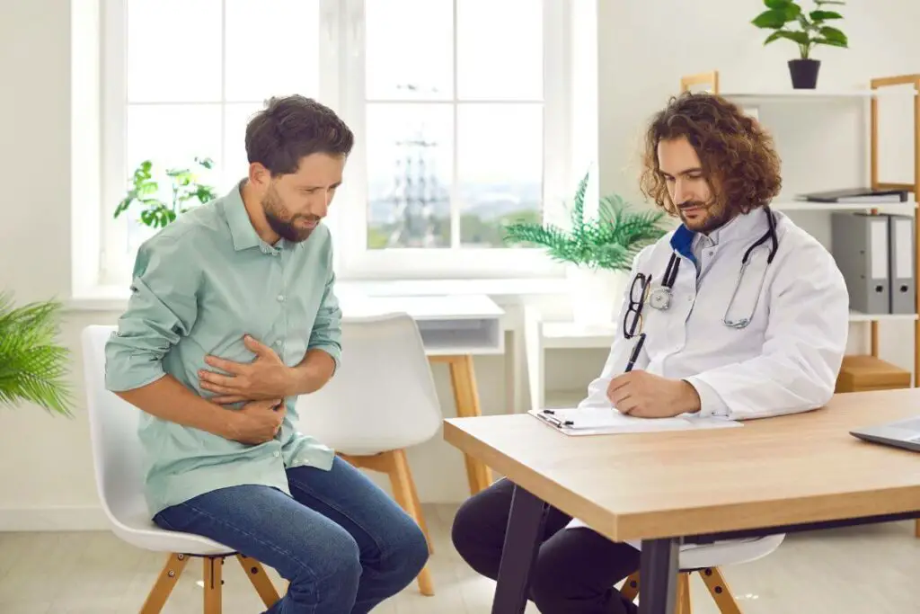 A man sitting in a chair with a stethoscope around his stomach, possibly indicating his need for ibs medication.