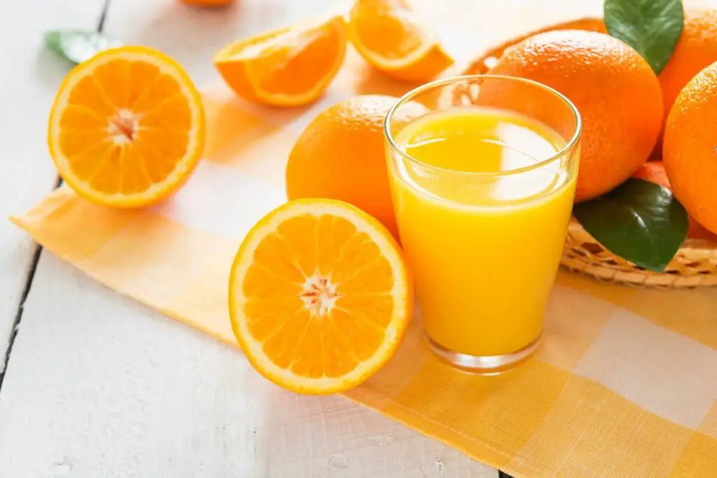 A glass of orange juice and oranges on a table, perfect for those with IBS.