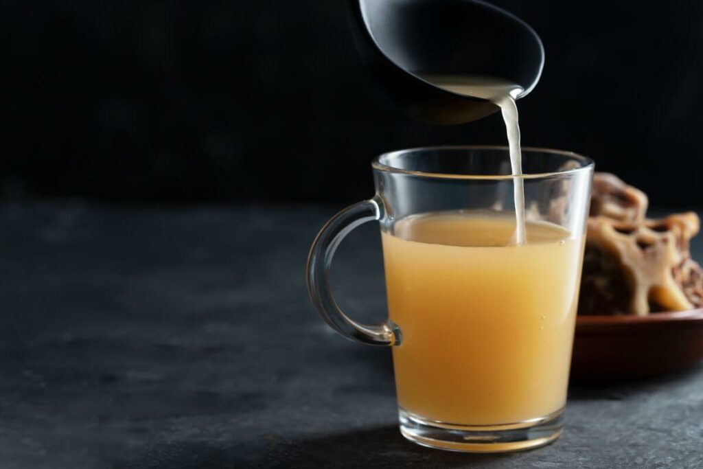 The best drink for IBS, a cup of orange juice, is gracefully poured into a glass.