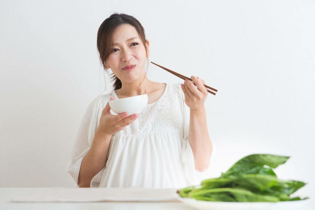 A pregnant woman peacefully enjoying a bowl of cooked greens with chopsticks, suitable for individuals with IBS.