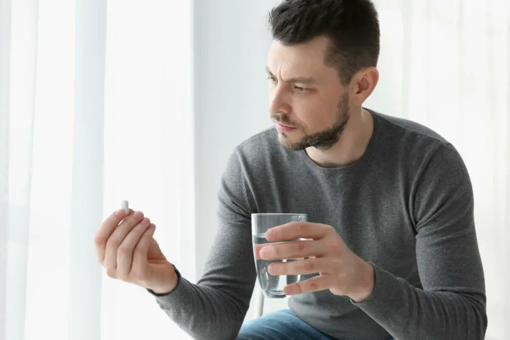 A man sitting on the floor with a glass of water, potentially taking ibs medication.