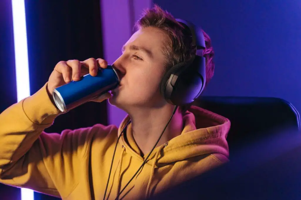 A young man enjoying a beverage from a can while listening to music on headphones.