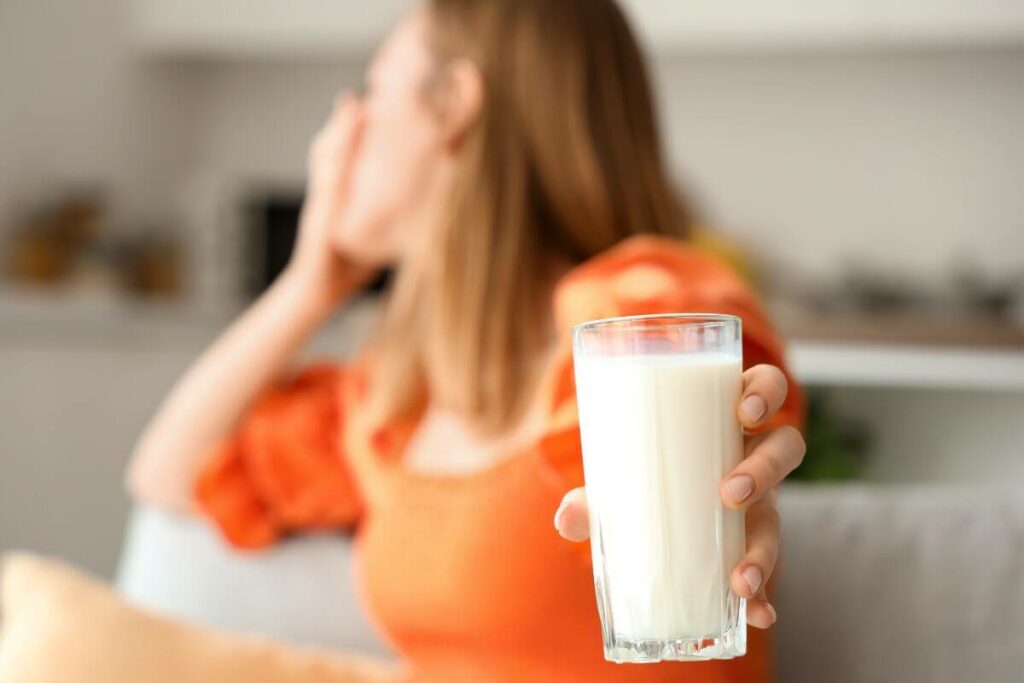 A woman holding up a glass of milk, symbolizing the connection between dairy and digestive discomfort related to IBS.