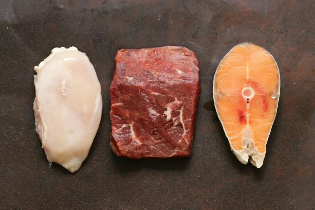 Three pieces of meat and salmon on a dark background.