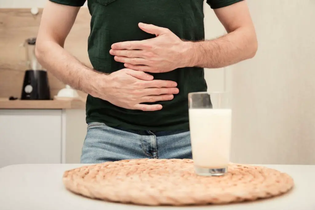A man with ibs holding his stomach in front of a glass of milk.