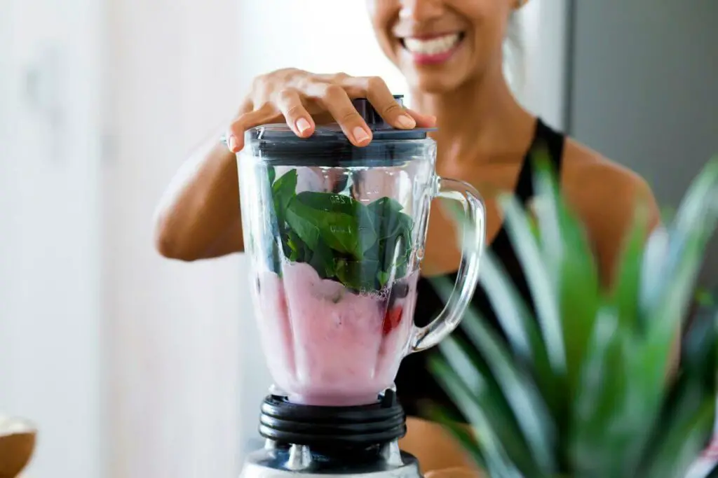 A woman is making a smoothie, one of the best drinks for ibs, in a blender.