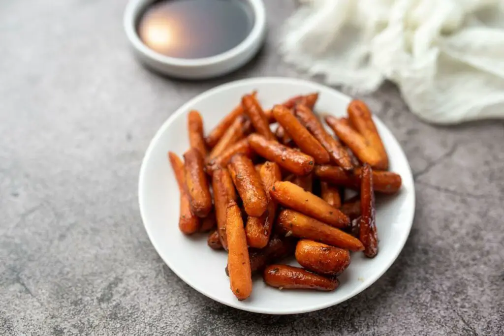 Roasted carrots on a plate next to a bowl of sauce for raw vegetables and IBS.