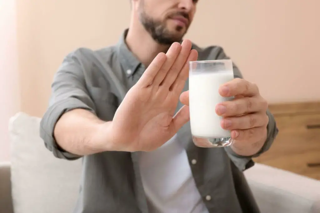A man with lactose intolerance is holding a glass of almond milk and making a stop sign.