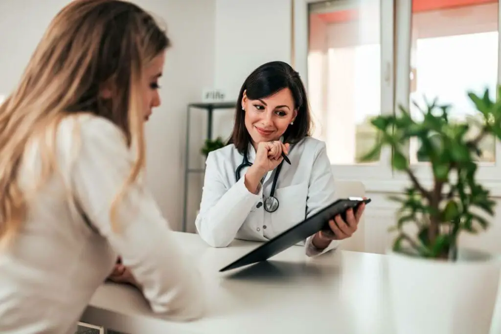 A female doctor is discussing dietary options with a female patient who has been diagnosed with irritable bowel syndrome (IBS) at a consultation table.