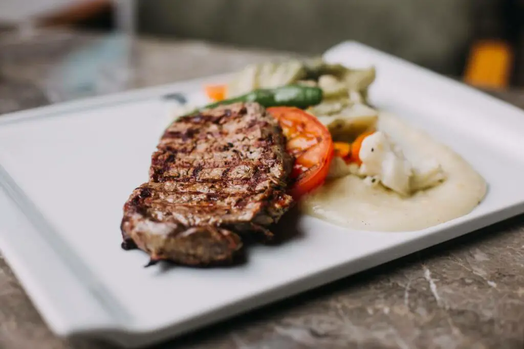 A steak with vegetables on a white plate, suitable for individuals with IBS and meat preferences.