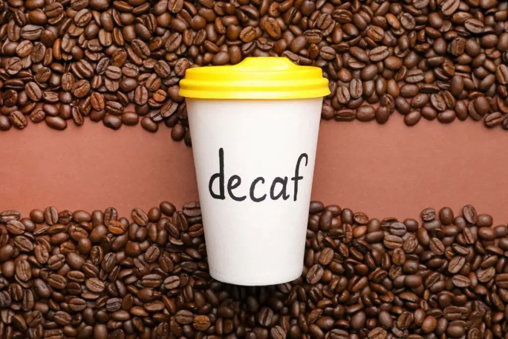 A coffee cup with the word decaf on it surrounded by coffee beans, the best drink for IBS.