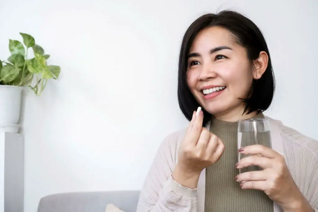 Asian woman holding a glass of water and smiling while taking ibs medication.