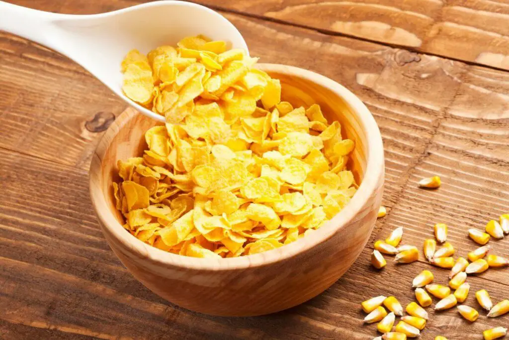 Whole grain corn flakes in a bowl on a wooden table.