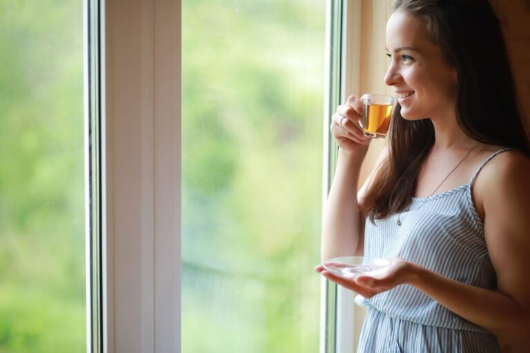 A woman enjoying a warm cup of tea while looking out of a window.