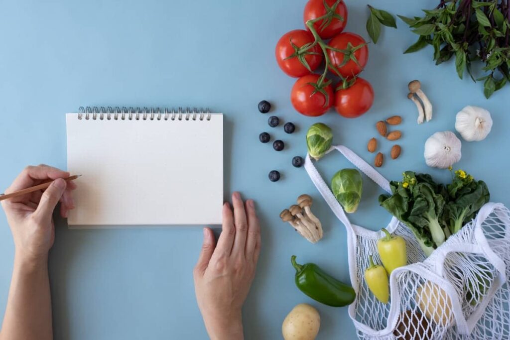 A woman is writing on a notepad next to a bag of vegetables.