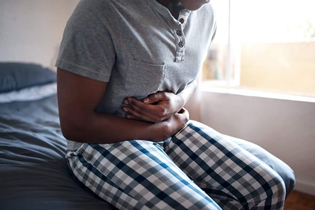 A man sitting on a bed experiencing abdominal pain.