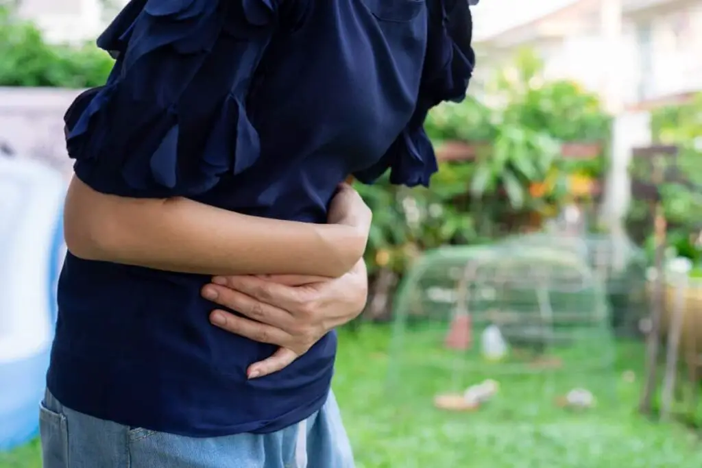A woman is experiencing gastrointestinal discomfort in a garden, possibly related to IBS-C.