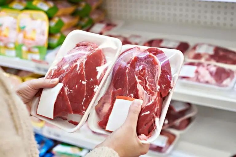 A woman is holding a tray of meat in a grocery store, considering options suitable for individuals with IBS while shopping for meat.